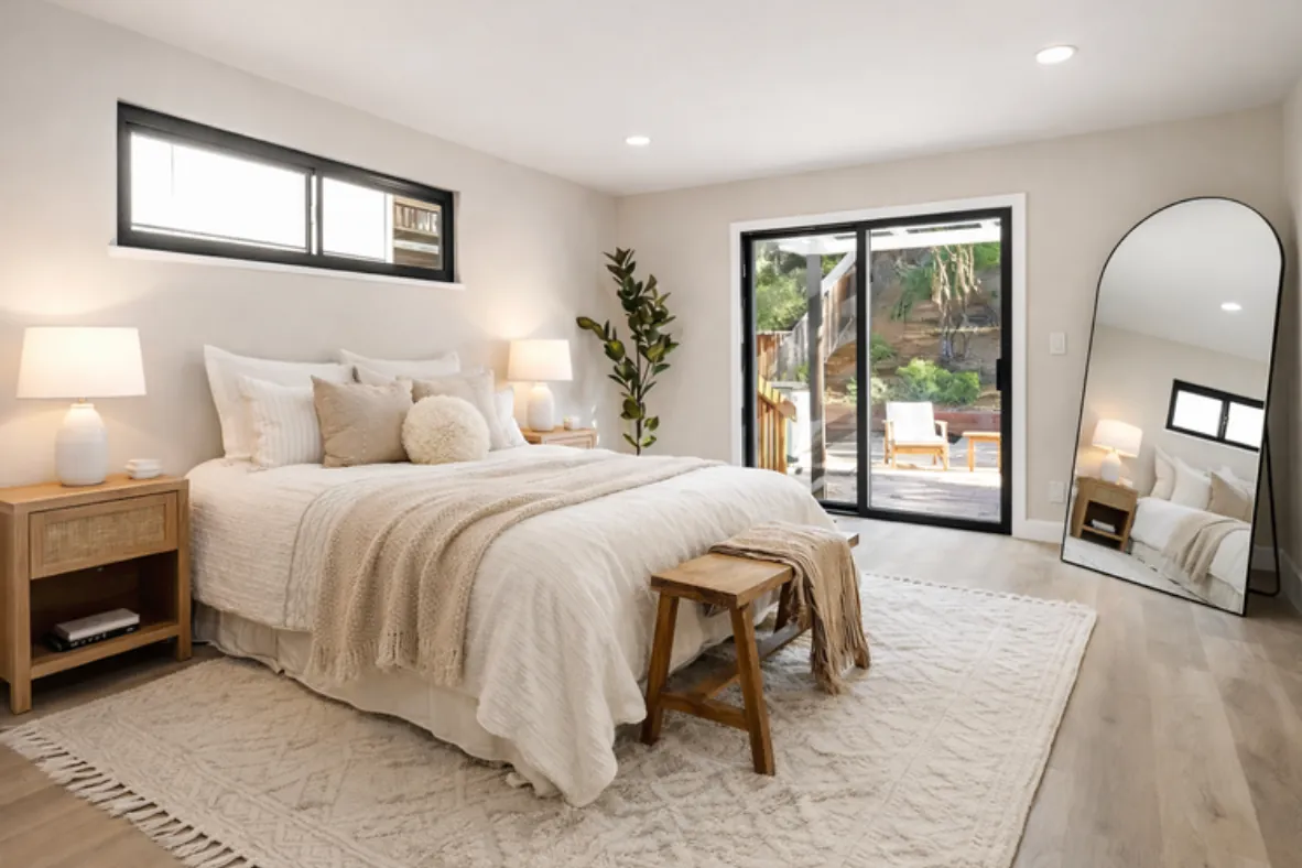Staged Oakland bedroom with cream bedding, a wood bench, an arched floor mirror and a sliding door