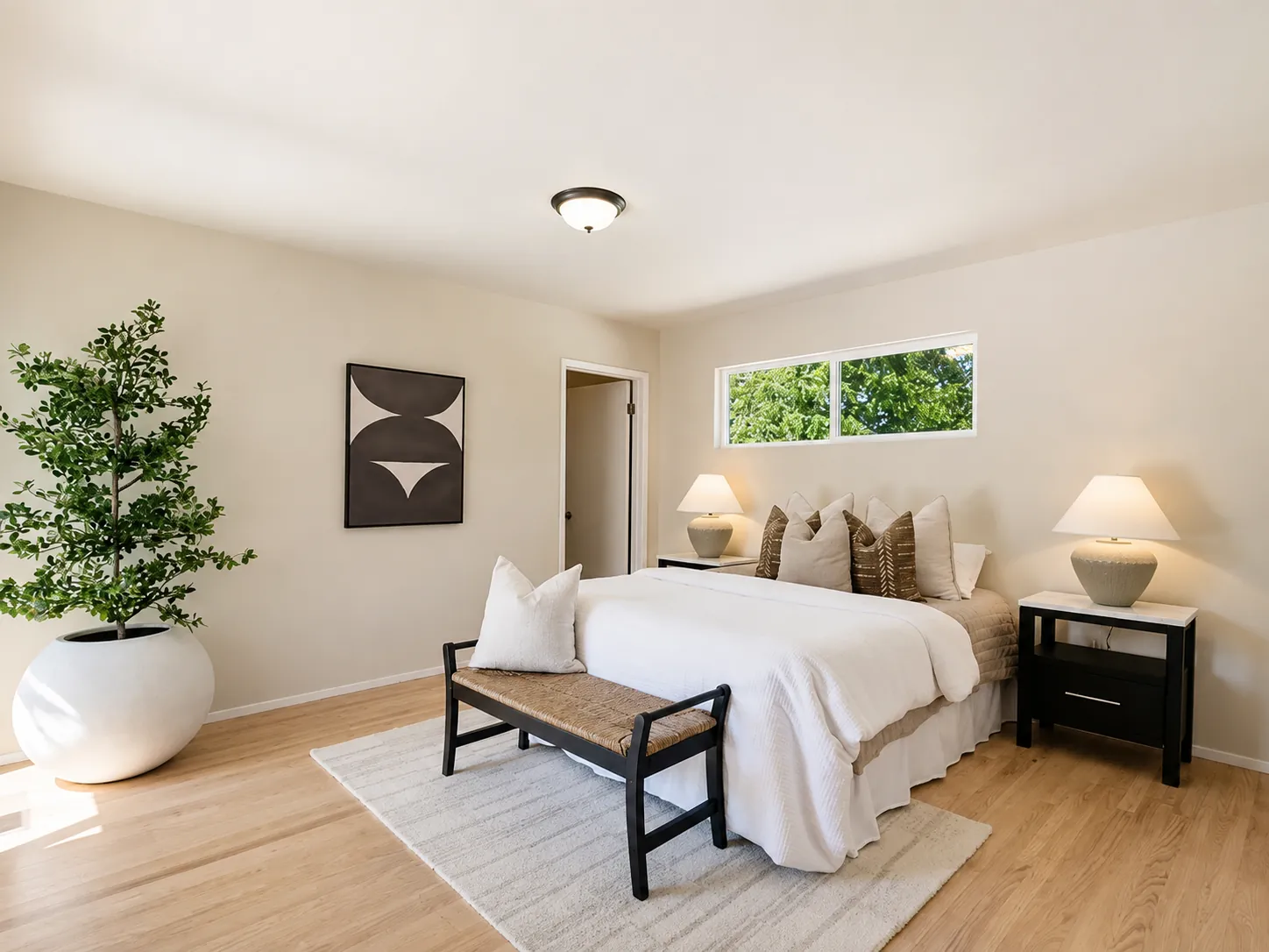 Staged bedroom with white bedding, black nightstands and a woven bench at the foot of the bed
