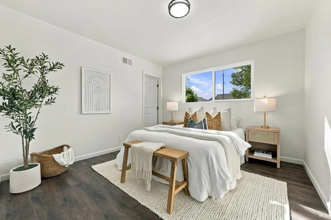 Staged bedroom with white bedding, a wood bench, a jute rug and an olive tree