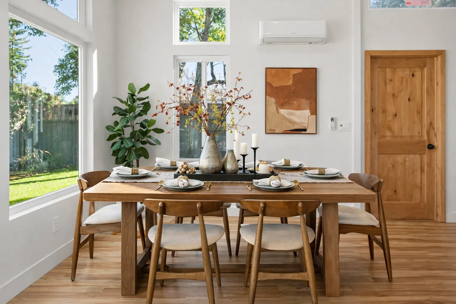 Staged dining room with a wood table set for autumn, rust-toned art and a natural wood door