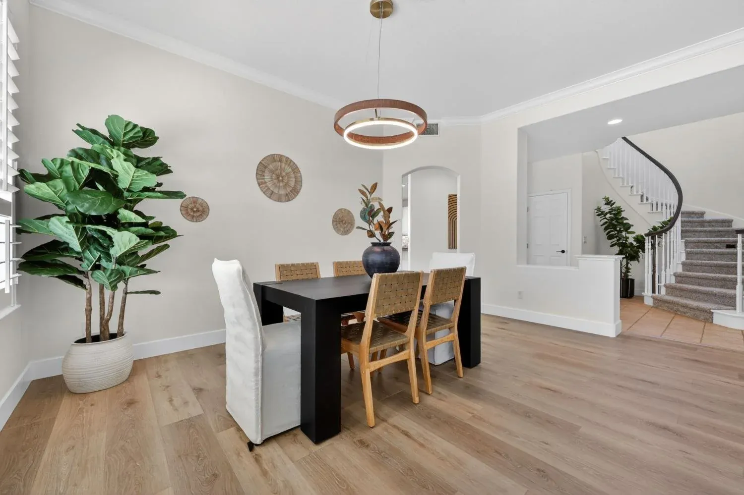 Staged dining room with a black table, woven chairs and a curving staircase beyond