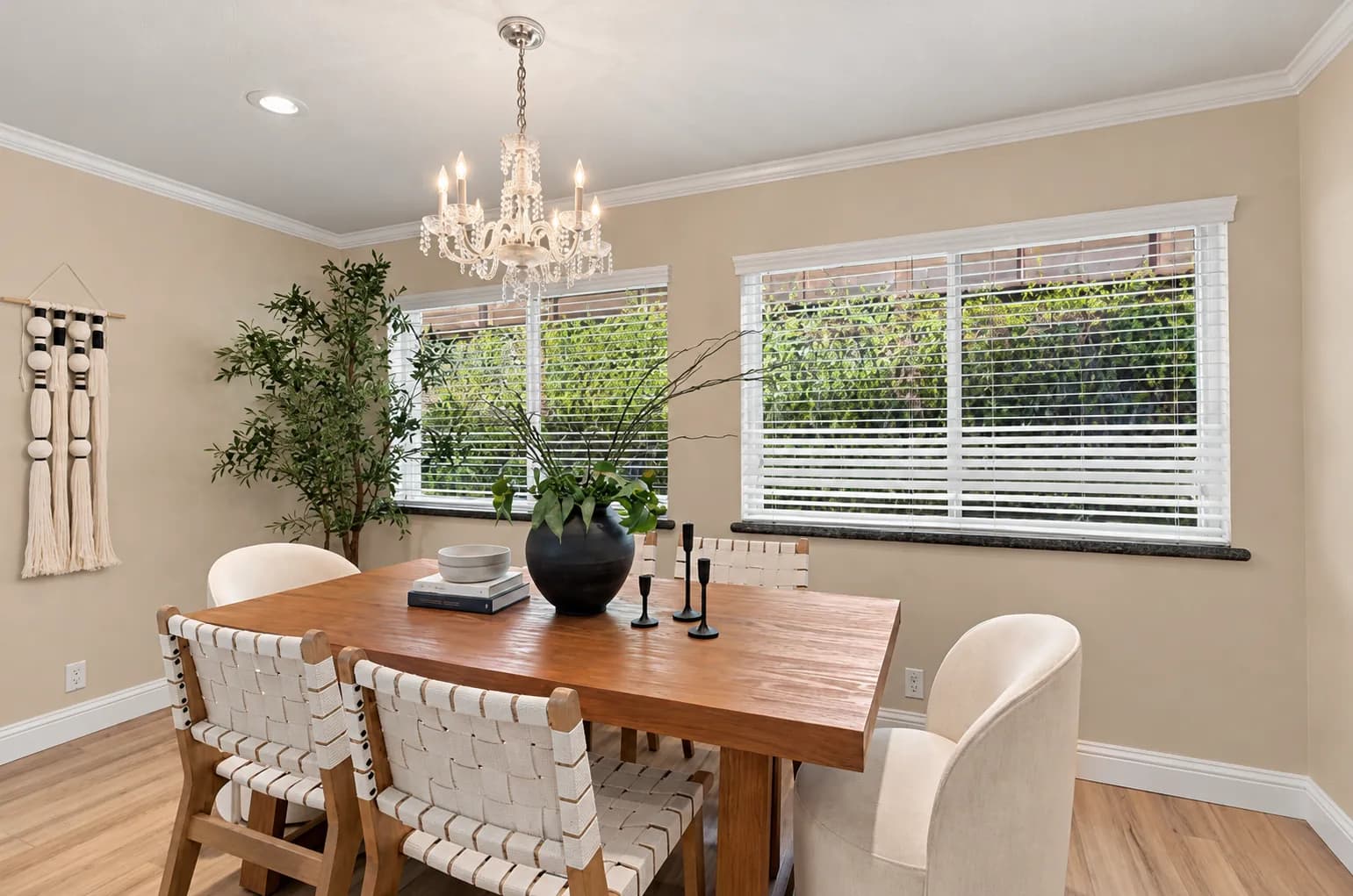 Staged dining room with a wood table, white woven chairs and a crystal chandelier