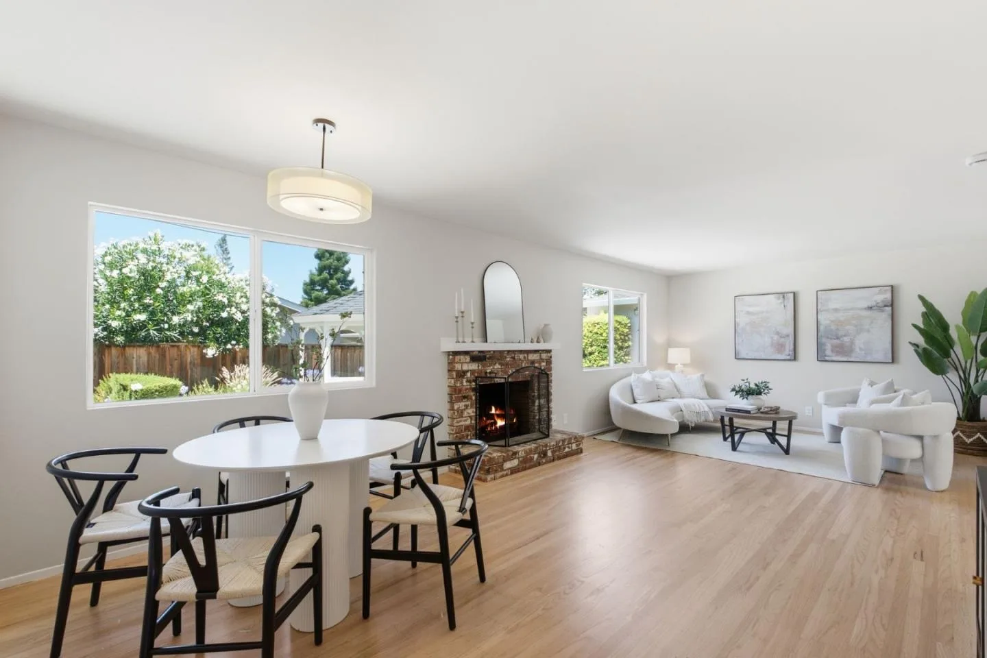 Staged Los Altos home with a white round dining table, wishbone chairs, a brick fireplace and curved sofas beyond