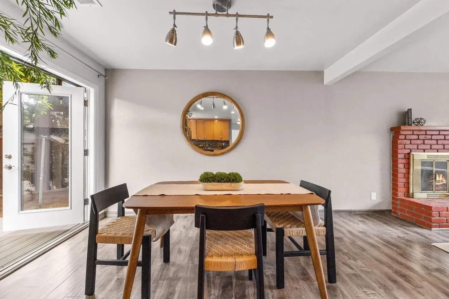 Staged dining area with a wood table, a red brick hearth and open patio doors