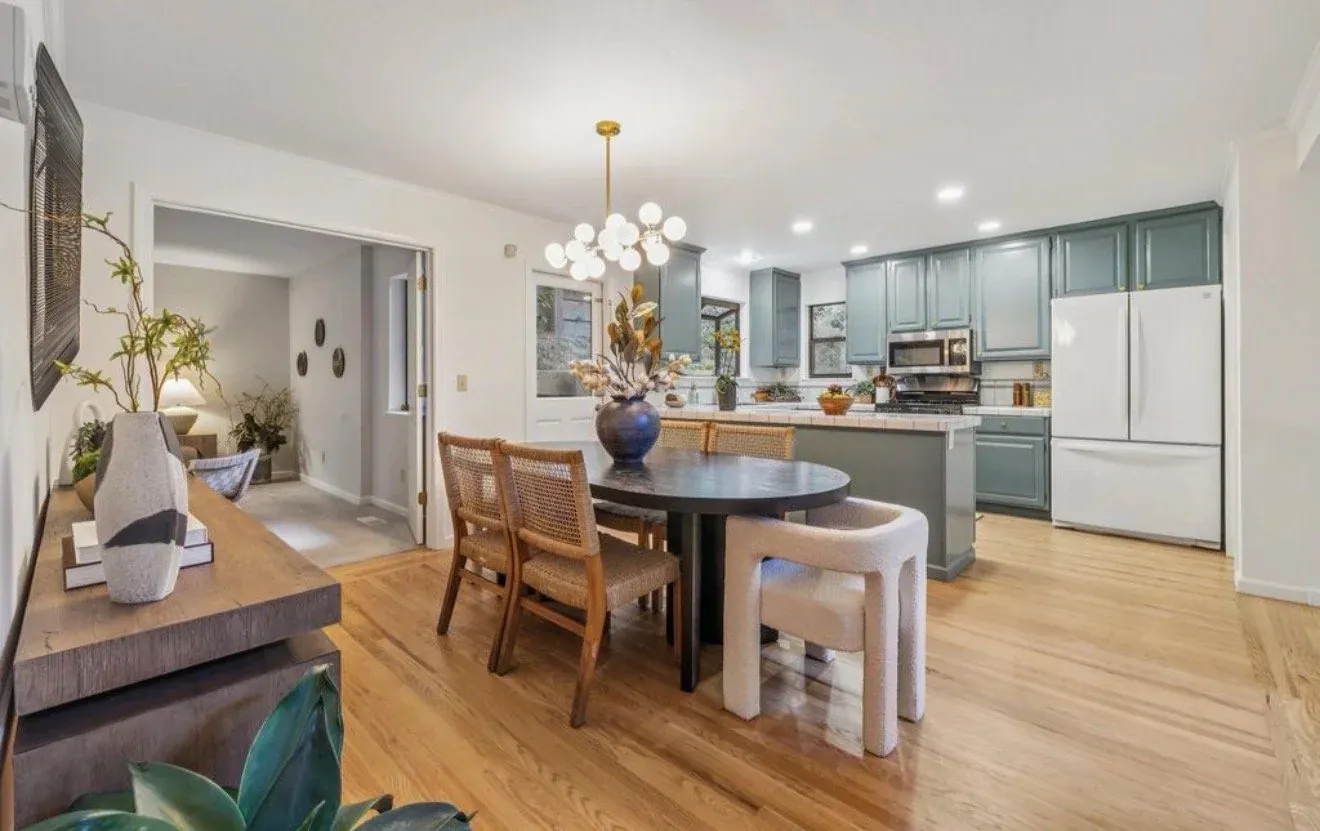 Staged dining area with a round black table in front of a sage green kitchen
