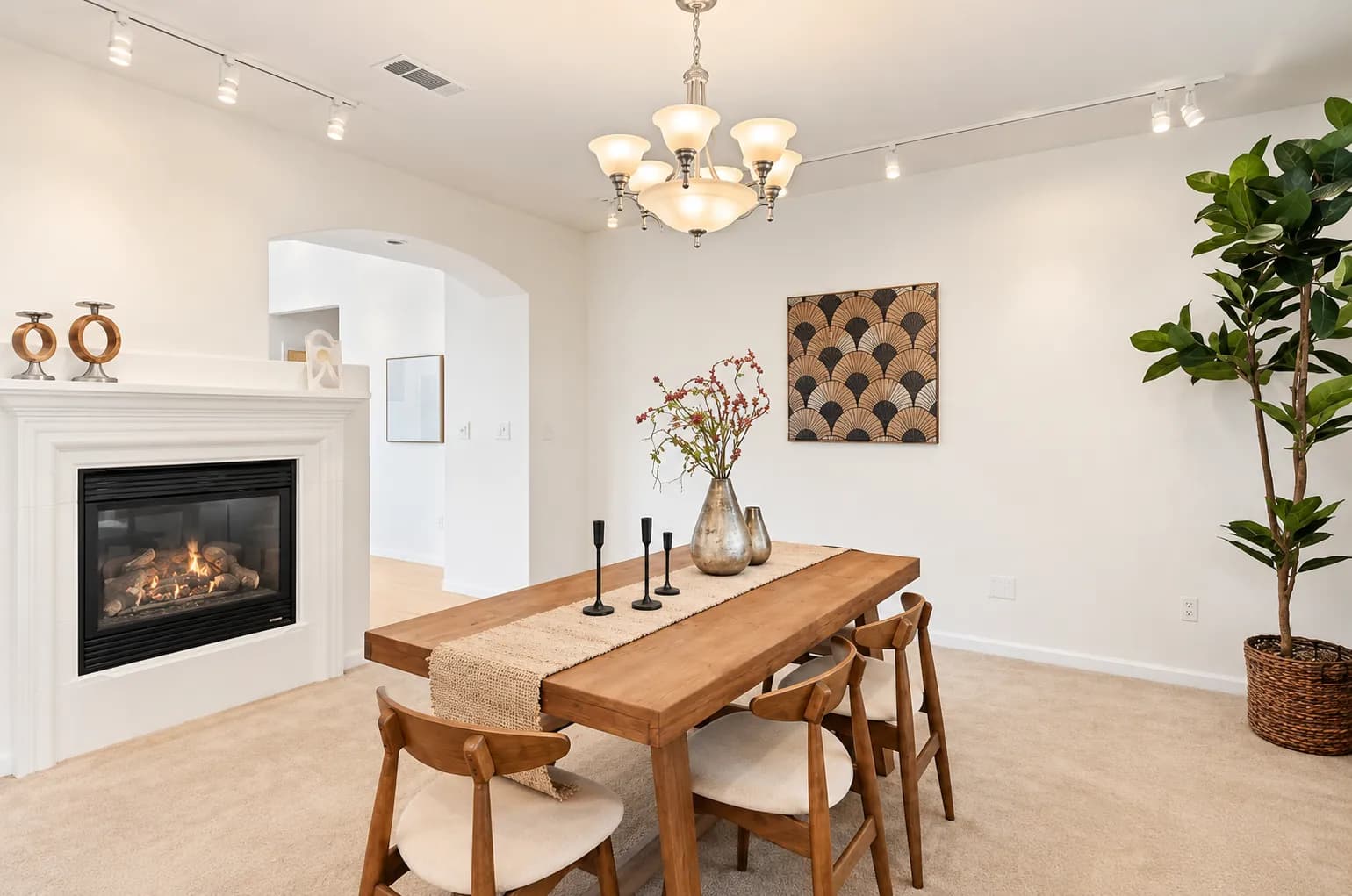 Staged dining room with a wood table, a white gas fireplace, a chandelier and a fiddle-leaf fig