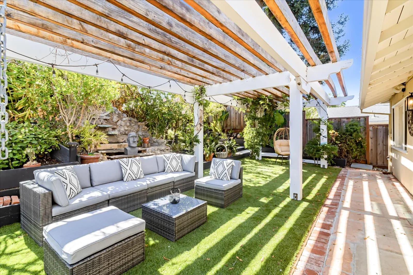 Staged backyard with a white pergola, wicker lounge seating and a green lawn
