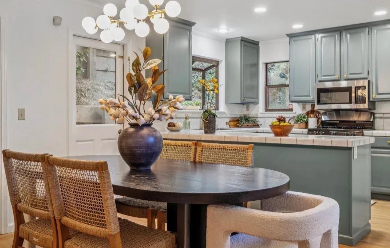 Staged kitchen with sage green cabinets and a dark round dining table in the foreground