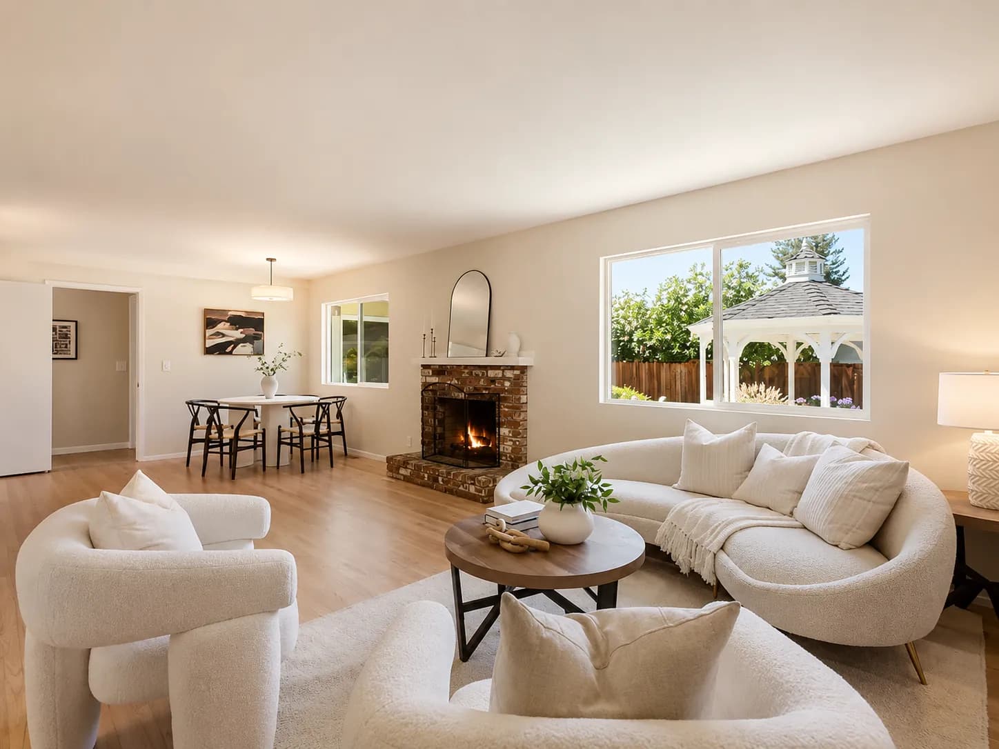 Staged living room with bouclé chairs, a curved cream sofa and a brick fireplace