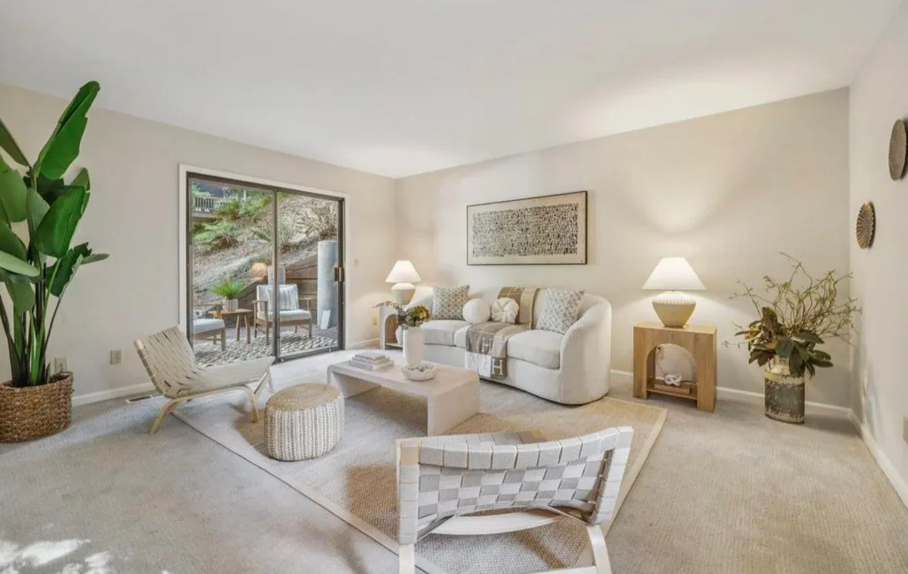 Staged carpeted living room with a cream sofa, woven chairs and sliding doors to the garden