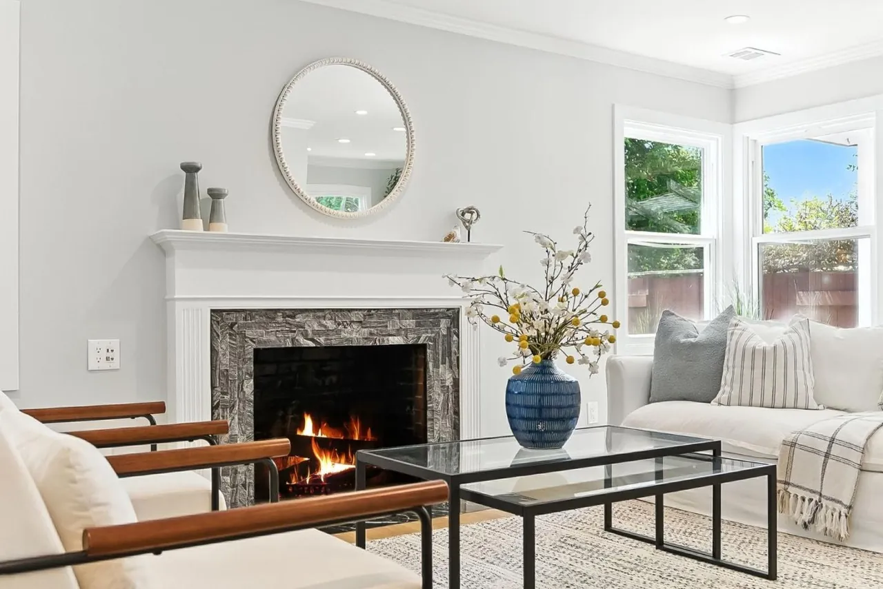 Staged living room with a marble fireplace, a glass coffee table, leather sling chairs and a round mirror