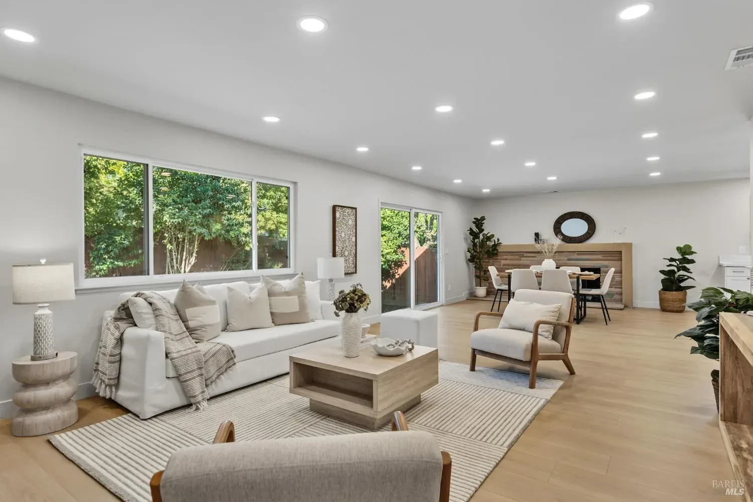 Staged living room with a neutral sofa and armchairs, with the dining area beyond