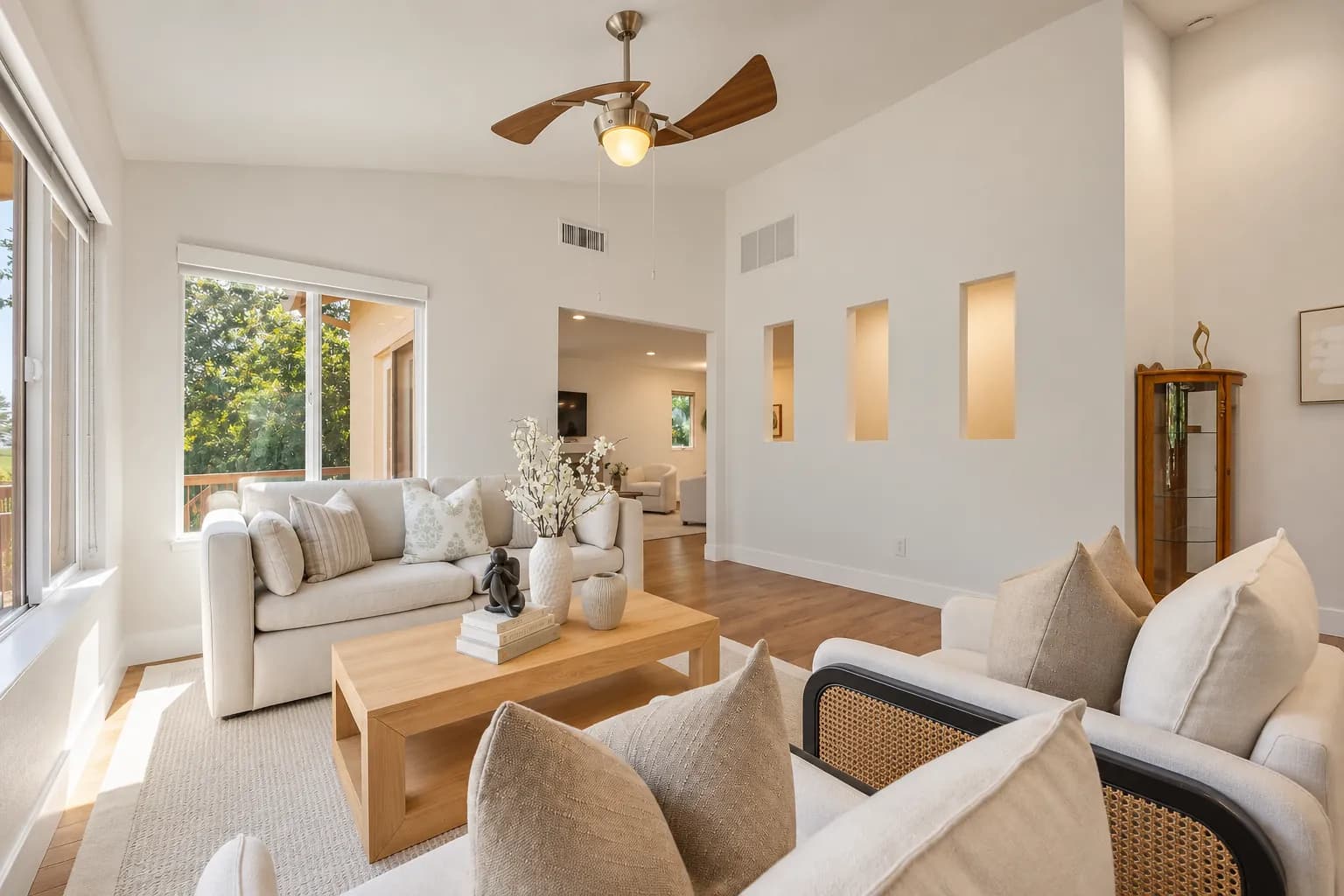 Staged living room with wall niches, a ceiling fan, a light wood coffee table and cane-back chairs